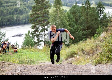 Sportler läuft bergauf im Hintergrund Bergfluss, Berge und Wald. Sprint-Rennen. Schnelle Bewegungen und Laufeffekte, Unschärfe Stockfoto