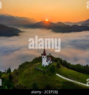 Šebrelje, Slowenien - Luftdrohnenansicht der wunderschönen Kirche des Hl. Ivan (Sv. Ivan Cerkev) bei Sonnenaufgang mit riesigen Morgennebel unten das Tal