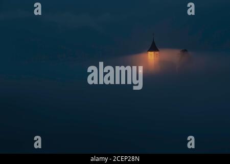 Jamnik, Slowenien - beleuchtete charmante St. Primoz-Kirche an einem nebligen Sommerabend Stockfoto