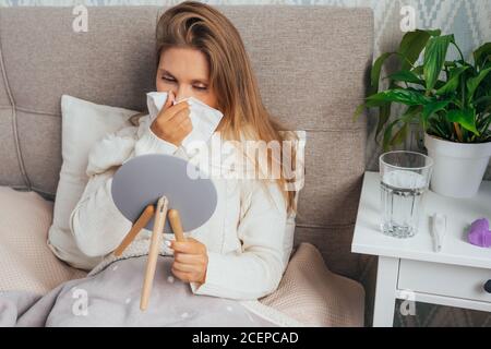 Eine junge Frau bläst ihr Taschentuch in der Nase und hat Symptome von chronischer Sinusitis, saisonaler Allergie, Erkältung oder Grippe Stockfoto