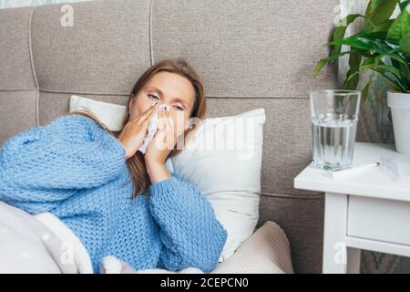 Junge Frau leidet zu Hause an Grippe. Frau bläst ihre Nase hält Gewebe Taschentuch, mit Symptomen einer chronischen Sinusitis, saisonale Allergie, Stockfoto