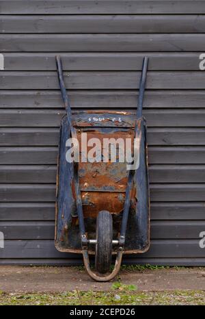 Rusty gebrauchte Schubkarre stand gelehnt an einen Schuppen bereit für die Arbeit. Stockfoto