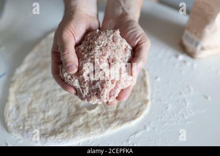 Männliche Hände halten Hackfleisch auf dem Hintergrund des Teiges. Stockfoto