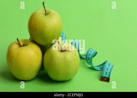 Sport und gesunde Regime Symbole. Diät und Sport-Regime Konzept. Äpfel in hellgrüner Farbe und verdrehtes Maßband auf grünem Hintergrund. Maßband in cyanfarbener Farbe nahe saftige Früchte, Nahaufnahme Stockfoto