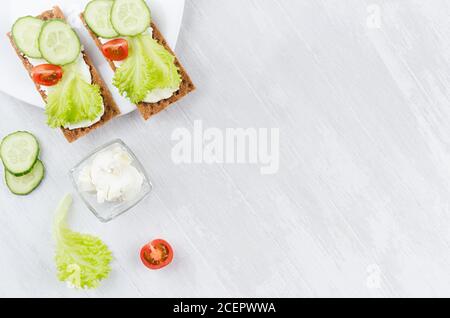 Frische Frühlingsvitamine Sandwiches von flachen Cerealien Roggen trockene Chips Brot mit grünem Salat, Gurke, Tomaten, Frischkäse auf weißem Holztisch, Top vie Stockfoto