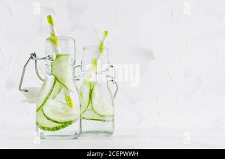 Frische Sommercocktails mit grüner Gurke, Limonade, Stroh in Joch-Flaschen auf elegantem, hellweißem Holzbrett und Gipswand. Stockfoto