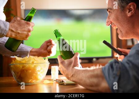 Mann zu Hause mit Freunden beobachten Spiel im Fernsehen mit Bier und Chips Stockfoto