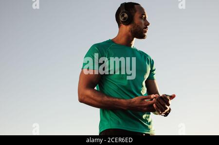 Nahaufnahme eines afro-amerikanischen Mannes im T-Shirt, der im Freien steht. Männlicher Athlet, der während des Trainings Musik hört. Stockfoto