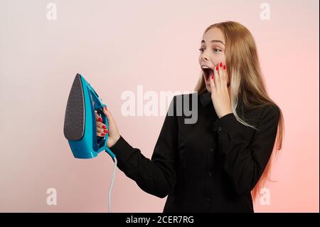 Schreiende junge Mädchen mit Eisen in der Hand isoliert auf rosa Hintergrund Stockfoto