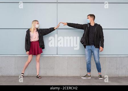 Junges, glückliches, liebevolles Paar, das Masken trägt und Hände mit der sozialen Distanz hält Stockfoto