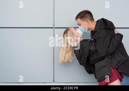 Junges, glückliches, liebevolles Paar, das Masken trägt und küsst Stockfoto