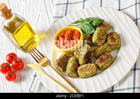 Gebackene Brokkoli auf einem weißen Teller mit Marinara-Sauce auf einem Holztisch mit Zutaten auf einem Schneidebrett und goldenem Besteck, horizontale Ansicht von Stockfoto