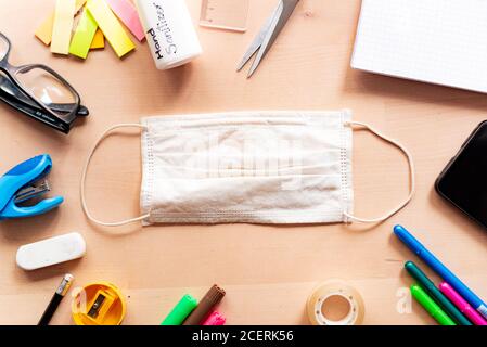 Nahaufnahme der Gesichtsmaske auf Holz Schreibtisch im Klassenzimmer mit Handy und Block Notizen und Bildungseinrichtung. Konzept der Prävention von covid in der Schule Stockfoto