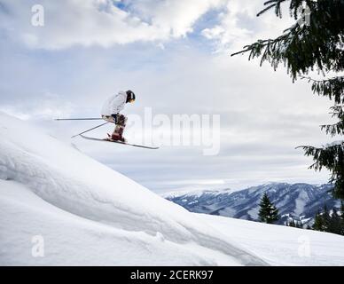 Seitenansicht Momentaufnahme des Skifahrers, der extremen Sprung von einem verschneiten Hang führt und gegen den erstaunlichen Himmel und die Bergkette im Hintergrund fliegt. Speicherplatz kopieren. Konzept der Ski- und Wintersport-Aktivitäten. Stockfoto