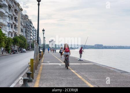 Thessaloniki, Griechenland - 12. September 2016: Mädchen mit rotem Rucksack Fahrrad entlang der Küste vor Stadtbild Hintergrund reiten. Das Stadtleben am Morgen. P Stockfoto