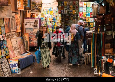 Touristen, Einkäufer und ein Mann auf einem Motorrad treffen sich im Souk in der Medina, Marrakesch Stockfoto