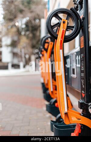 Die Öko-Fahrzeuge. Orange Elektroroller in einer Reihe an der Stadt Transport Mietschalter befindet. Draußen, Straße. Vertikale Ausrichtung. Stockfoto