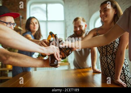 Klirrende Flaschen. Junge Gruppe von Freunden trinken Bier, Spaß haben, lachen und feiern zusammen. Frauen und Männer mit Biergläsern. Oktoberfest, Freundschaft, Zweisamkeit, Glückskonzept. Stockfoto