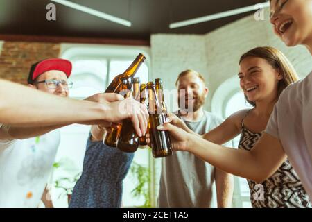 Klirrende Flaschen. Junge Gruppe von Freunden trinken Bier, Spaß haben, lachen und feiern zusammen. Frauen und Männer mit Biergläsern. Oktoberfest, Freundschaft, Zweisamkeit, Glückskonzept. Stockfoto
