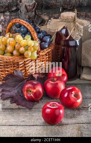 Schwarze und weiße Trauben mit roten Äpfeln und frischem Saft Auf dem rustikalen Tisch und vor dem Holz Stockfoto