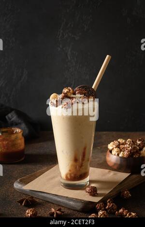 Schmackhafter Bananen-Milchshake garniert Karamell, Schlagsahne auf dunklem Hintergrund. Vertikales Format Stockfoto
