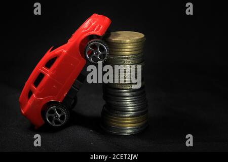 Geld sparen für ein Auto. Bankwesen, schnell. Spielzeugauto und Münzen auf schwarzem Hintergrund. Miniatur-rotes Auto-Modell auf wachsenden Stapel von Münzen. Finanzierung und Autokredit. Stockfoto