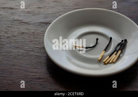 Eine weiße Untertasse mit mehreren verbrannten Streichhölzern auf einem Holztisch. Nahaufnahme der Küchengeräte aus Porzellan. Selektiver Fokus. Stockfoto