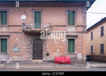 Rote alte ruinierte Sofa links auf dem Bürgersteig in einem Öffentliche Straße eines Dorfes im Süden Italiens Stockfoto