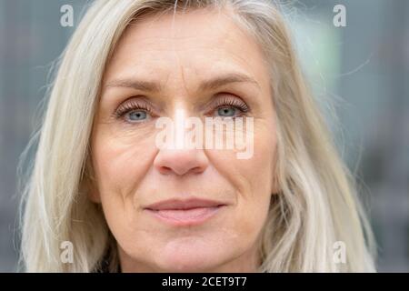 Close up 7/8 Portrait von einem attraktiven blauen Augen reife Frau mit langen blonden Haaren direkt auf das Objektiv Stockfoto