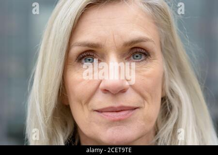 Close up 7/8 Portrait von einem attraktiven blauen Augen reife Frau mit langen blonden Haaren direkt auf das Objektiv Stockfoto