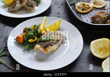 Gegrillter Fisch mit Zitrone, Kräutern und Rosmarin. Gebratene Fischfilets auf einem weißen Teller. Schöne Präsentation des Essens. Rucolla Salat und Karotten. Stockfoto