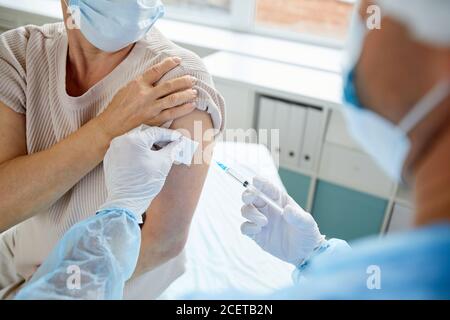 Moderne medizinische Mitarbeiter, die Injektion mit Impfstoff an nicht erkennbare weibliche Patientin in Schulter, High-Angle-View-Aufnahme Stockfoto