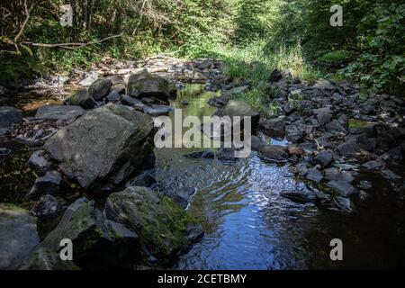 Flusslauf übersät mit Felsen mit Wasserfall im Siegerland Stockfoto