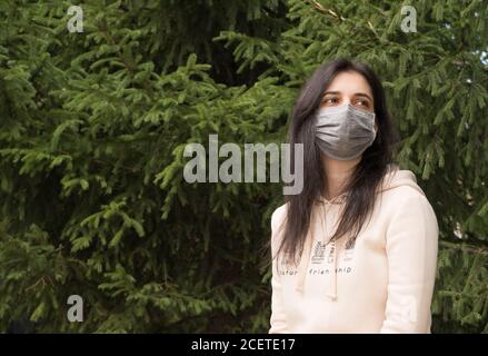 Ein Mädchen in einem Park, das eine medizinische Maske trägt. Gesundheitswesen, Coronavirus, Pandemie, kovid19. Das Tragen von Masken an öffentlichen Orten. Eine Frau mit langen schwarzen h Stockfoto