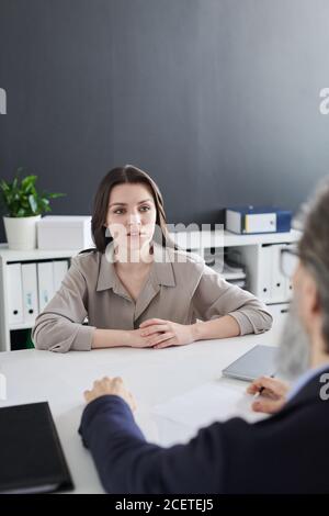 Schöne junge Frau, die vor einem nicht erkennbaren HR-Manager sitzt Im Bürozimmer mit Vorstellungsgespräch Stockfoto