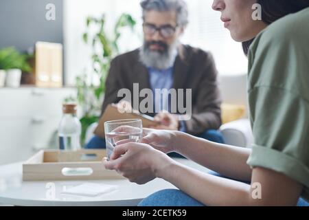 Leidvolle Frau, die ein Glas Wasser hält und versucht, sich zu beruhigen Während der Therapie-Sitzung im Psychologischen Büro Stockfoto