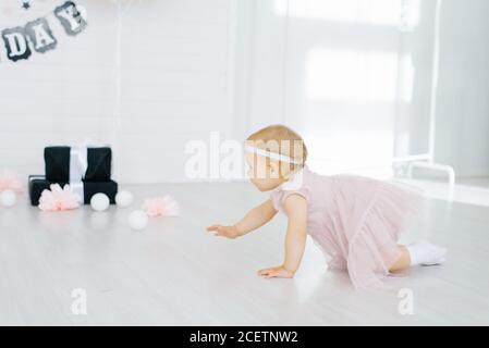 Ein einjähriges Mädchen in einem rosa Kleid kriecht auf dem Boden im Kinderzimmer Stockfoto