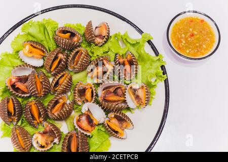 Jakobsmuscheln in einem weißen Gericht mit würziger Sauce auf dem Tisch dampfen. Stockfoto