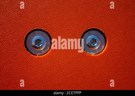 Textur einer orangefarbenen Kunststoffplatte mit zwei Sternschrauben. Die Platte hat ein Interessantes Muster. Stockfoto