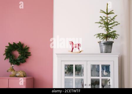 Weihnachtsbaum in einem Metall-Eimer, vintage Holz roten Spielzeug Pferd auf einer weißen Kommode im Inneren des Wohnzimmers, dekoriert für Weihnachten und Neu Stockfoto