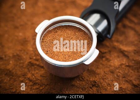 Auf dem Hintergrund des gemahlenen Kaffees befindet sich ein Halter aus der Kaffeemaschine im Filter, der auch mit gemahlenem aromatischem Naturkaffee gefüllt ist. Die Proce Stockfoto