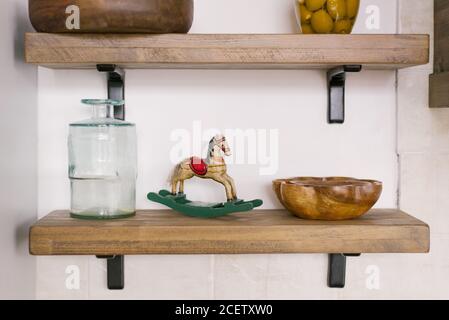 Auf einem Holzregal steht ein Vintage-Pferd aus Holz, neben einem Glas und einer Untertasse aus Holz. Küchenutensilien im Küchendekor Stockfoto