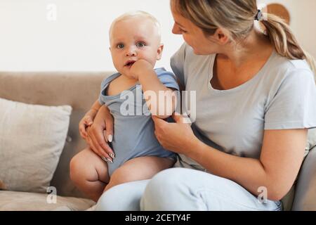 Horizontale mediuml Aufnahme der kaukasischen Frau sitzen auf dem Sofa verbringen Zeit mit ihrem schönen kleinen Baby, kopieren Raum Stockfoto