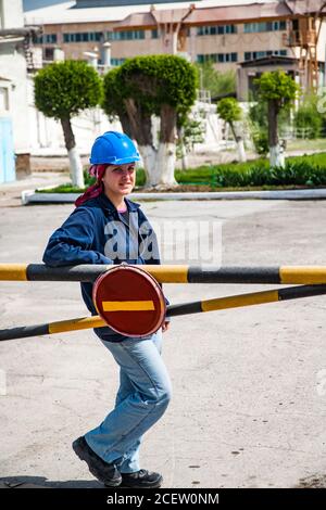 Taraz/Kasachstan - April 25 2012: Phosphordüngeanlage. Junge Arbeiterin Frau in blau Arbeitskleidung und Helm hinter der Barriere. Auf Bäumen und Indus Stockfoto