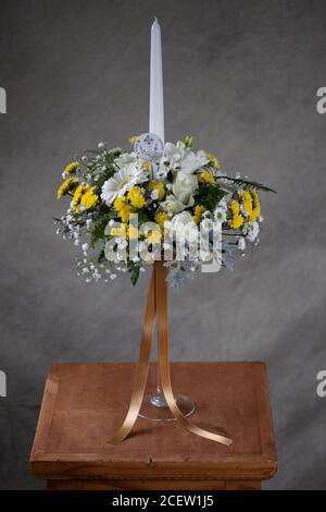 Erste heilige Kommunion Blumensträuße. Weiße Kerze mit weißen und gelben Blumen verziert. Graues Backgroud Stockfoto