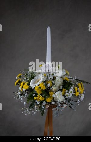 Erste heilige Kommunion Blumensträuße. Weiße Kerze mit weißen und gelben Blumen verziert. Graues Backgroud Stockfoto