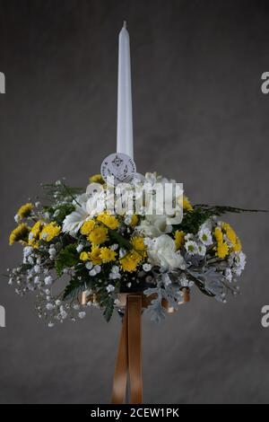 Erste heilige Kommunion Blumensträuße. Weiße Kerze mit weißen und gelben Blumen verziert. Graues Backgroud Stockfoto
