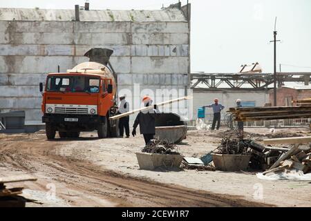 Taraz/Kasachstan - April 25 2012: Renovierung der Anlage für chemische Phosphordünger. Orangefarbener Betonmischer. Arbeiter, die Müll entfernen. Vorbereitung Stockfoto