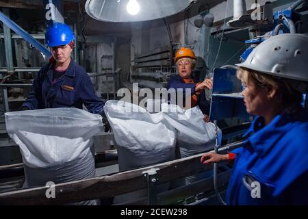 Taraz/Kasachstan - April 25 2012: Phosphordüngeanlage. Verpackungslinie Fabrik Werkstatt. Drei Arbeiterinnen in Schutzhelmen auf Förderband. Stockfoto