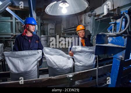 Taraz/Kasachstan - April 25 2012: Phosphordüngeanlage. Verpackungslinie Fabrik Werkstatt. Zwei Arbeiterinnen in orangefarbenen und blauen Schutzhelmen mit Stockfoto